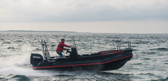Side view of a black and red HDPE boat and a Suzuki outboard motor, cruising on grey wavy seas with a focus on the boat and sea background