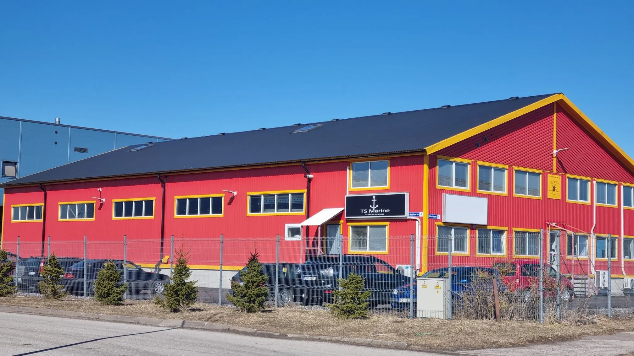 Industrial building with a striking red facade and yellow trim around the edges and on the gables. Office TSBoats.