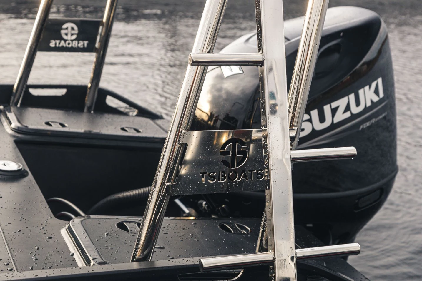Close-up of a sleek HDPE boat transom with a polished stainless steel ladder, Suzuki outboard engine, and TS Boats logo, with water droplets and a blurred water background.