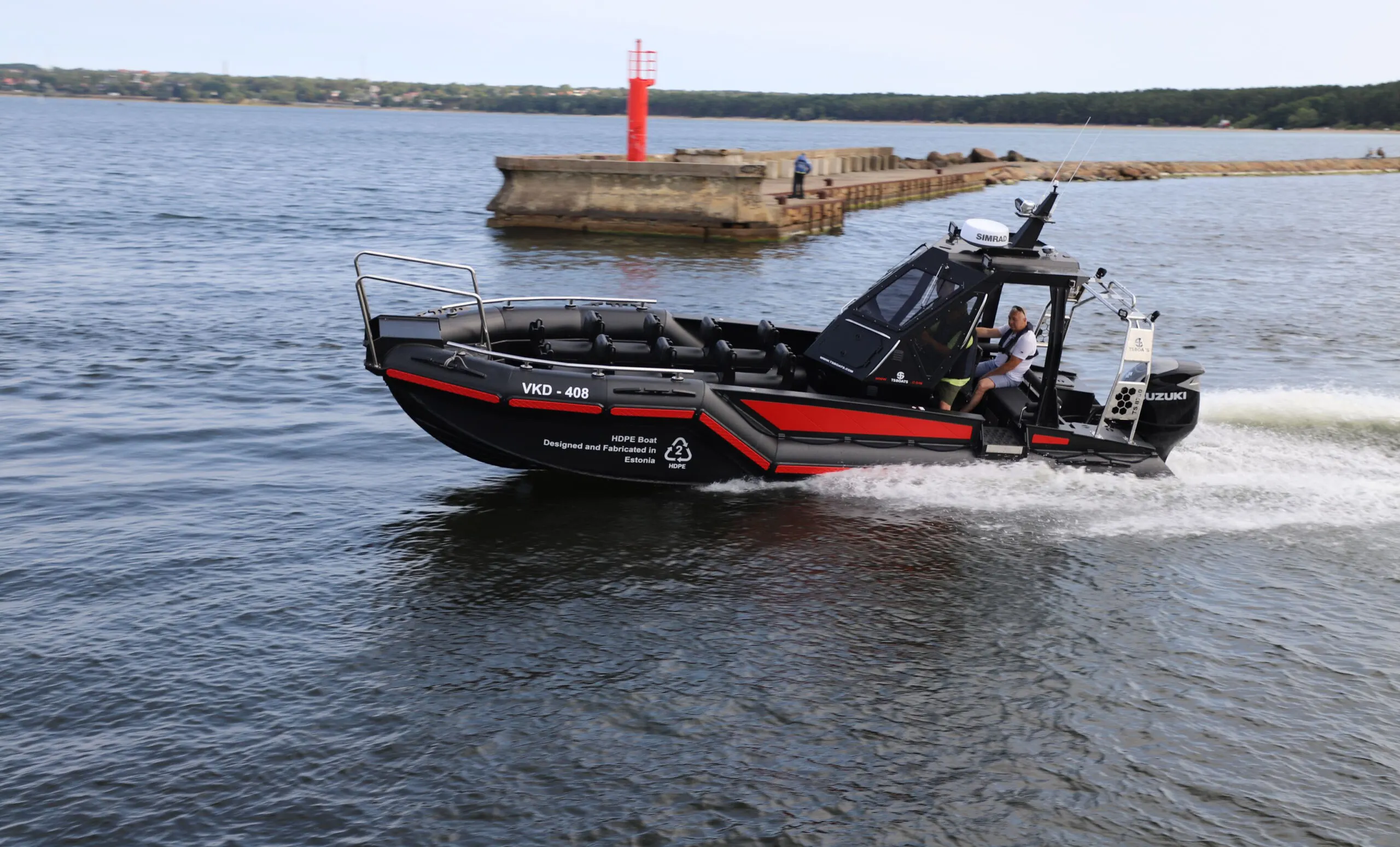 A man piloting a HDPE boat by TS Boats with a Suzuki outboard motor, making a sharp turn near a coastal jetty, a clear blue sky